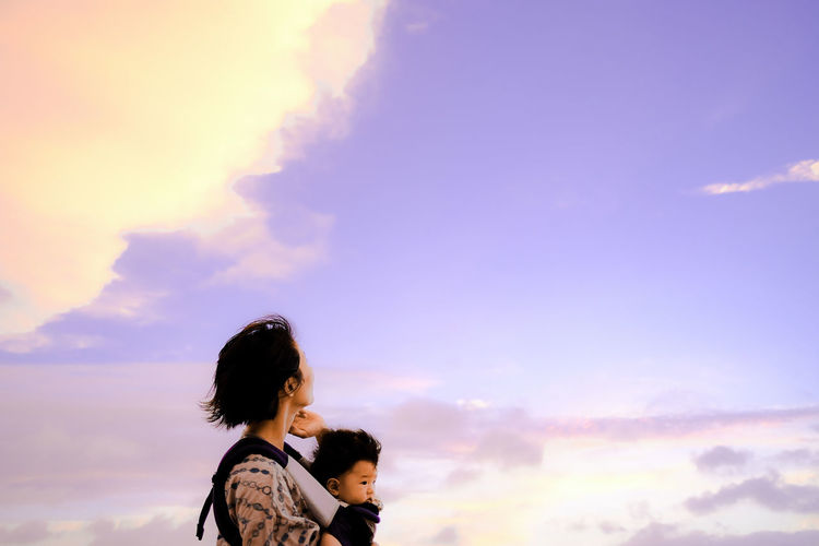 Side view of woman with arms raised against sky during sunset