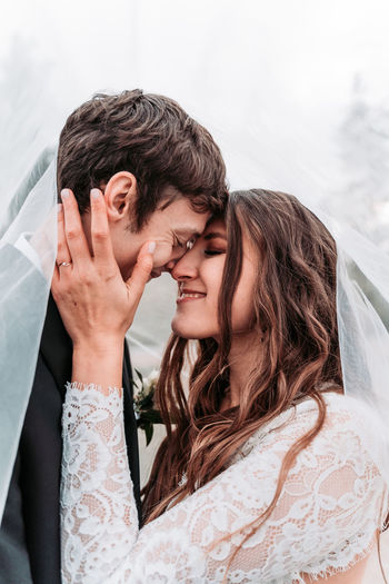 Close-up of newlywed couple with eyes closed romancing under veil