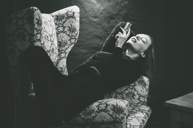 Young woman singing while lying on chair at home