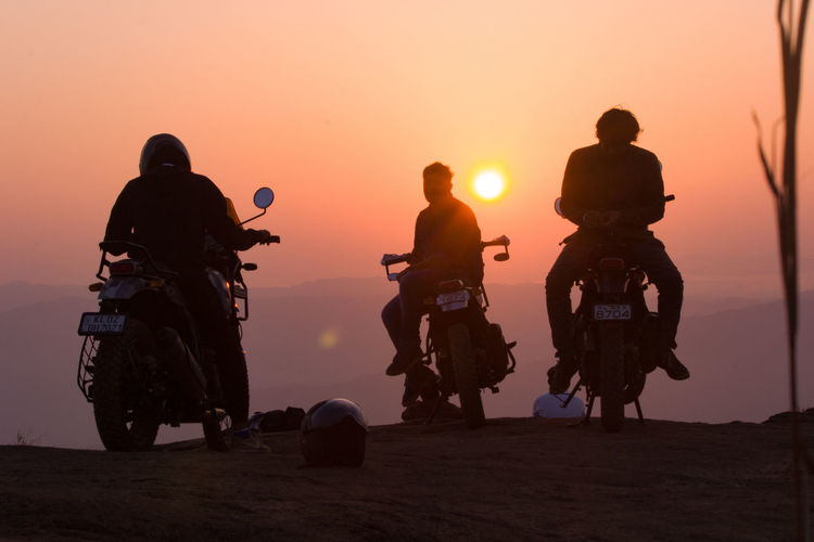 Silhouette people riding motorcycle against sky during sunset