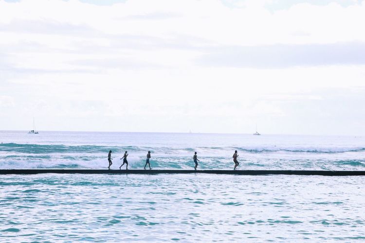 People walking on pier over sea against sky