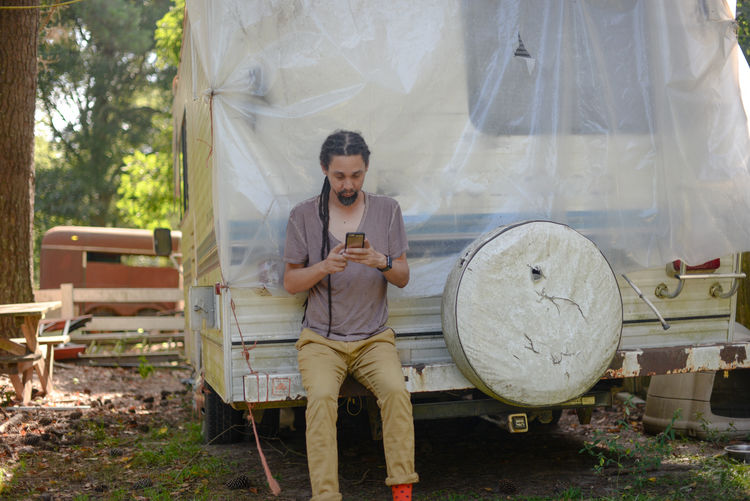 Man using mobile phone while sitting against motor home