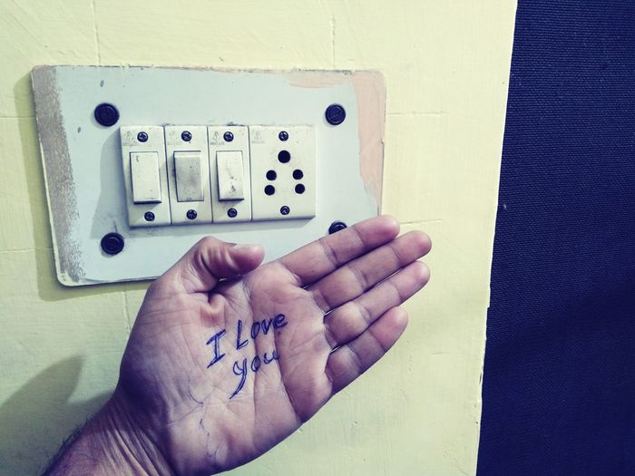 Cropped hand of man with text against electrical outlet