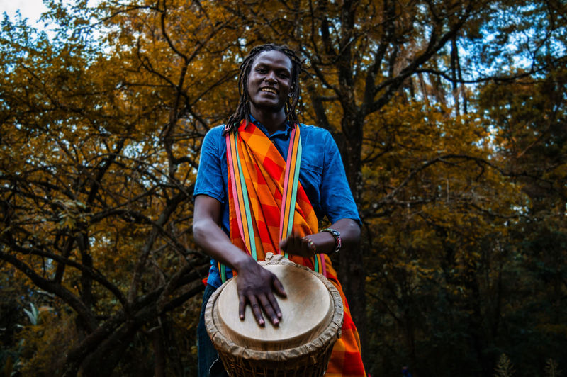 Full length of man holding umbrella while standing against trees, kenyan traditional masai