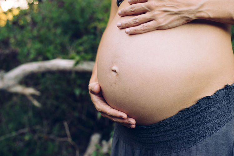 Midsection of pregnant woman with hands on stomach standing outdoors
