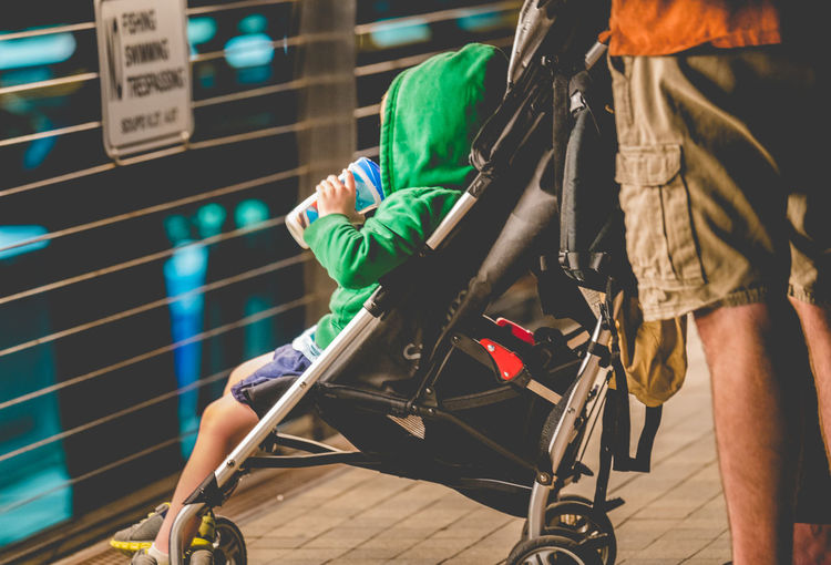 Midsection of man standing by son sitting in baby stroller
