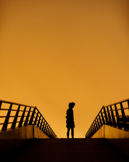 Silhouette man standing by railing against orange sky