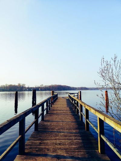 Pier over lake against clear blue sky
