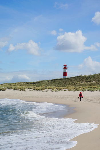Mid distance view of woman walking at beach against sky