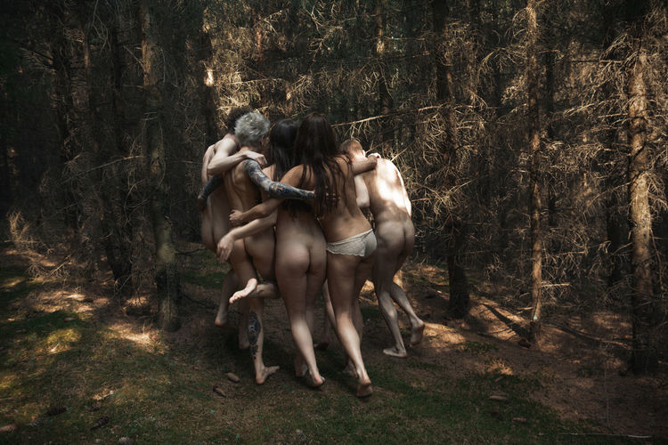 Cheerful naked people dancing in forest
