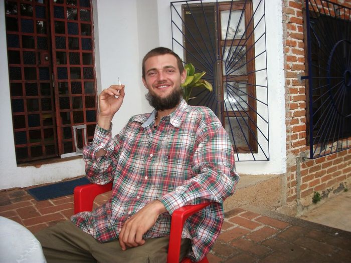 Portrait of smiling young man smoking cigarette on porch