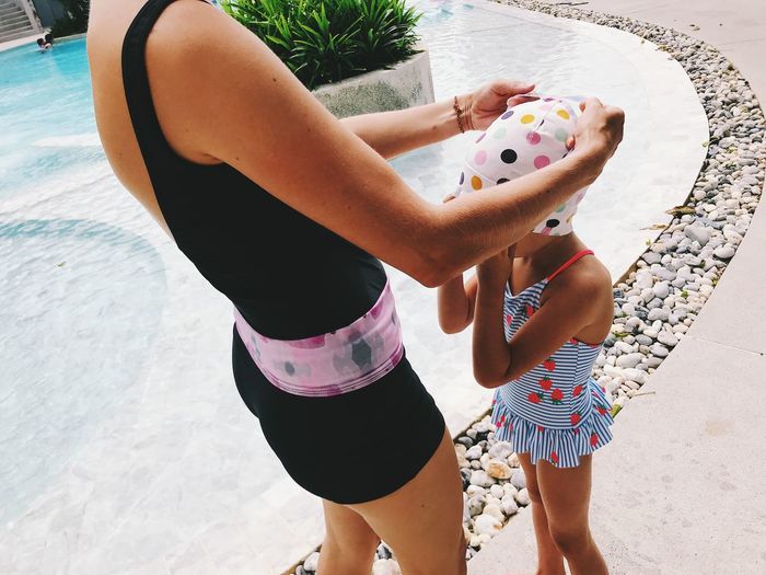 Midsection of mother assisting daughter in wearing swimming cap