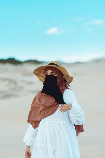 Muslim girl wearing hat, hijab and niqab walking in the desert against clear sky