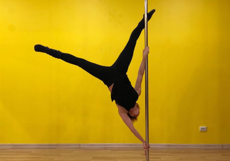 Full length of woman doing pole dancing against yellow wall