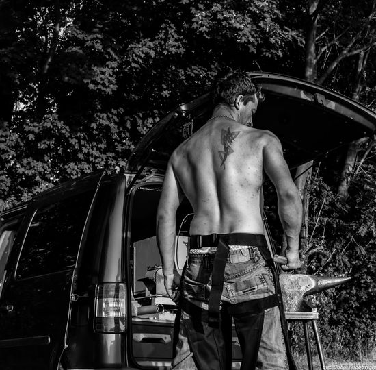 Rear view of shirtless man with tattoo standing by car