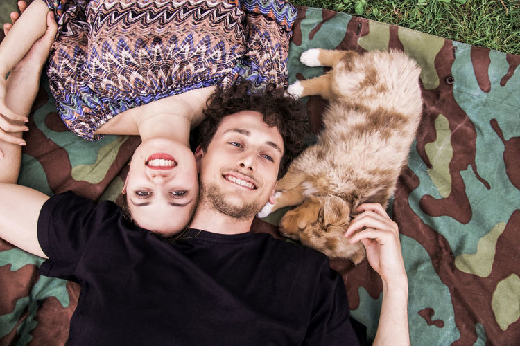 Portrait of young boyfriend and girlfriend lying down on a field with baby doggie smiling