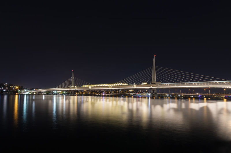 Illuminated bridge over river against sky at night