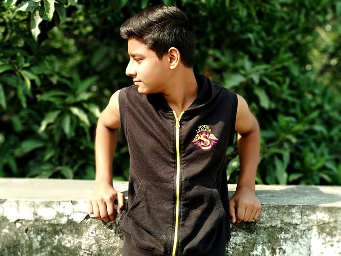 Boy looking away while standing against plants
