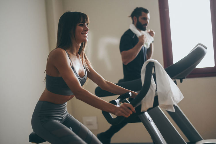 Determined young couple working out in gym. fit boy and girl doing cyclette and tapis roulant