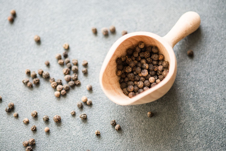 Directly above view of peppercorns in wooden scoop against gray background