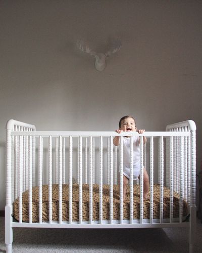 Cute smiling toddler baby standing in crib against wall at home