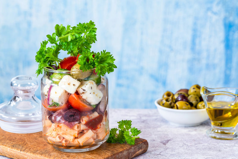 Salad with pasta, fresh vegetables, salami, olives and feta cheese in a jar - healthy lunch idea