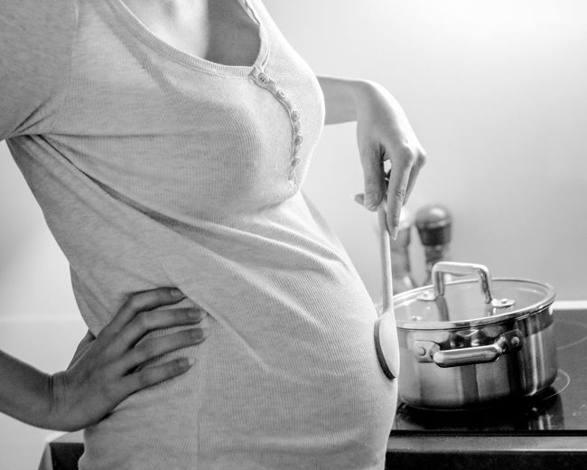Midsection of pregnant woman touching spatula on abdomen