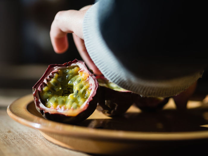 Close-up of hand holding passion fruit in plate