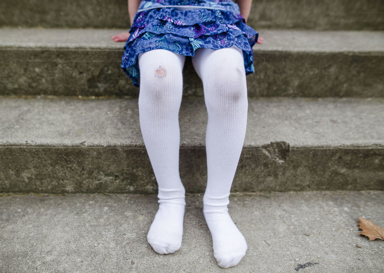 Bottom half of shoeless little girl with ripped tights and dirty knees