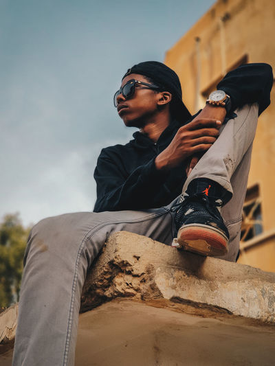Low angle view of young man wearing sunglasses against sky