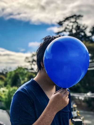 Midsection of man holding balloons against blue sky