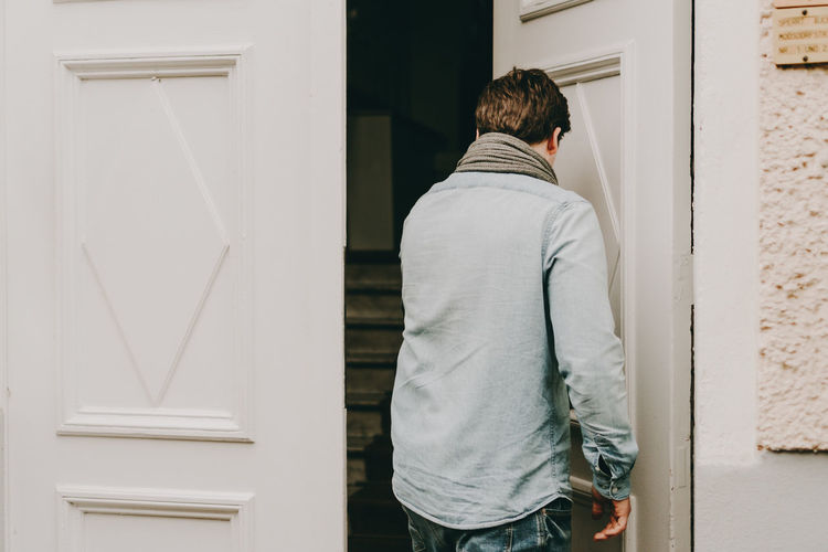Rear view of man standing against white door