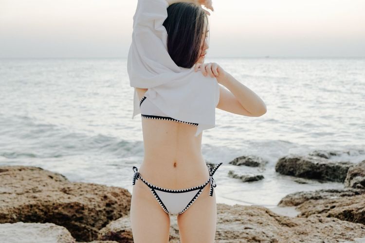Woman getting undressed while standing at beach against sky