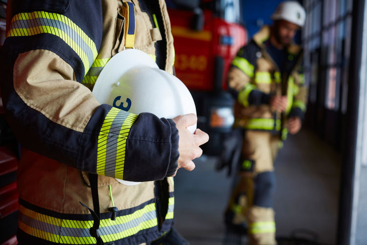 Midsection of female firefighter with protective helmet standing at fire station