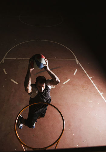 Basketball player in black and white sport clothes jumping and making dunk while training on sports ground