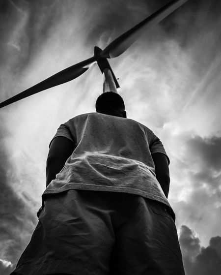 Rear view of man standing by windmill against cloudy sky
