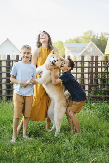 Cheerful family with their akita dog standing on grass in front of fence