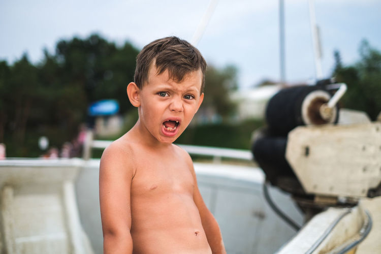 Portrait of shirtless boy screaming while standing at beach