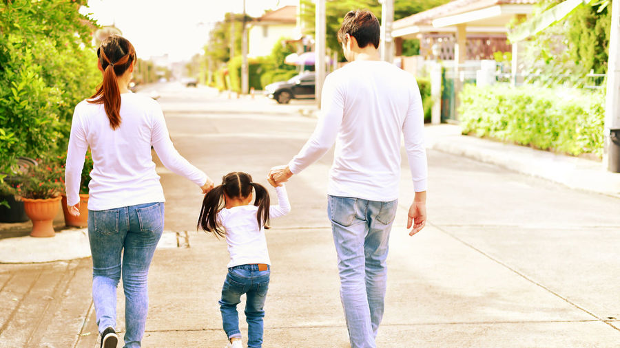 Rear view of parents holding daughter hands while walking on street