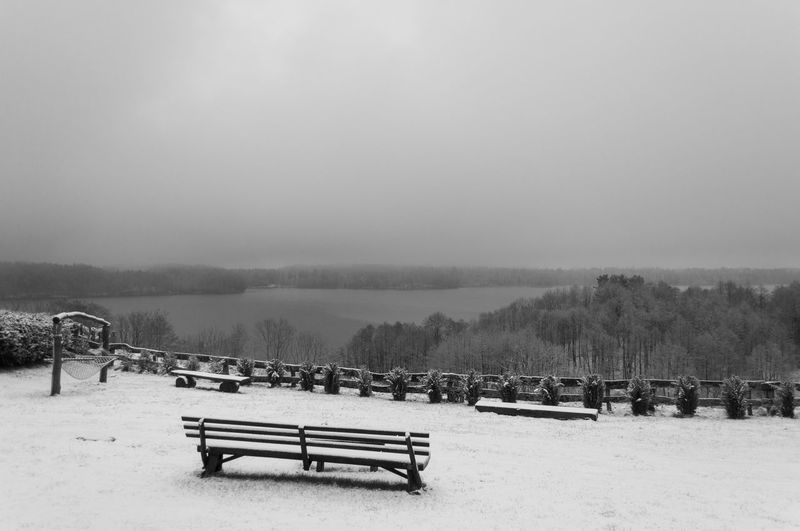 Benches on snow covered field against sky
