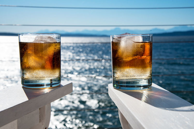 Close-up of whiskey glass on white armchair against sea