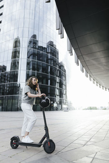 Woman with e-scooter and helmet, modern office buildings in the background