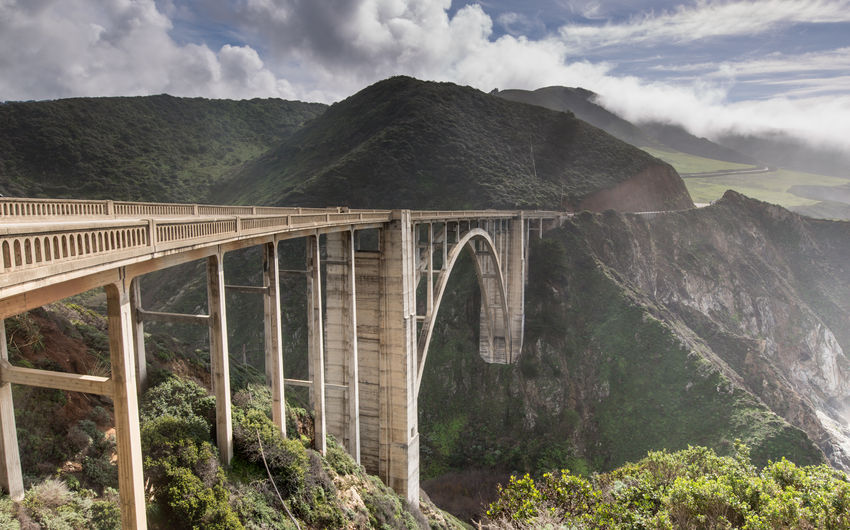 Arch bridge amidst mountains against cloudy sky
