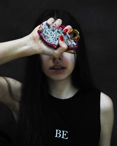 Close-up of young woman holding pitaya against black background