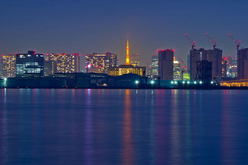 Illuminated buildings by river against sky at night