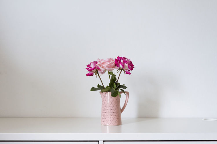 Pink flower vase on table against wall