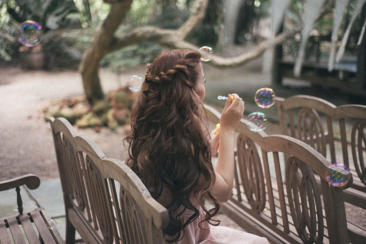 Woman blowing bubbles while sitting on bench at field