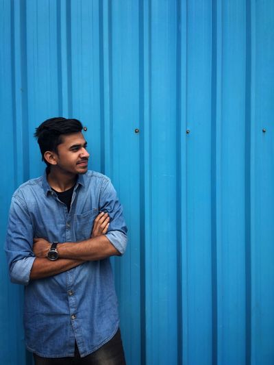 Young man looking away while standing against blue wall