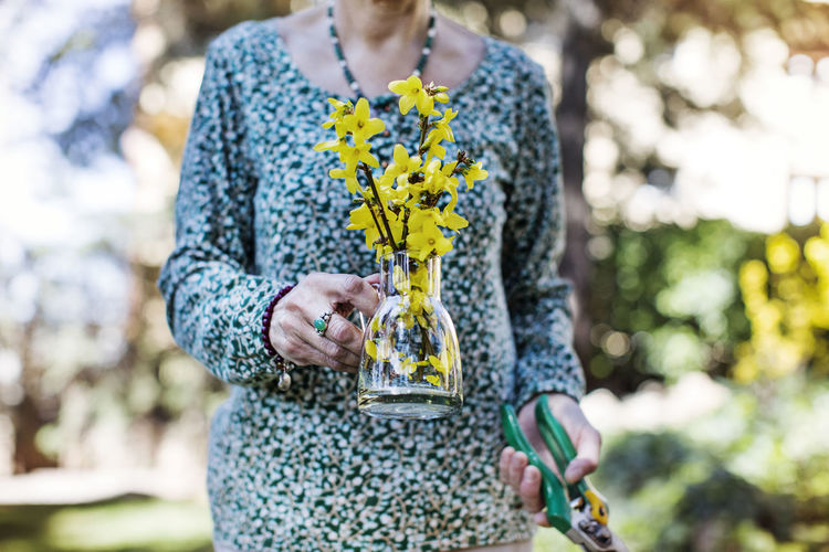 Midsection of senior woman holding flower vase and pliers at yard