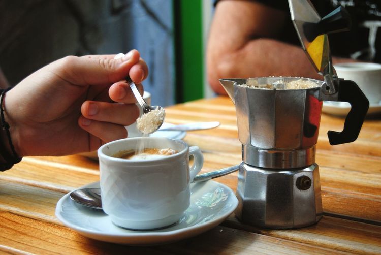 Close-up of hand adding sugar to coffee on table